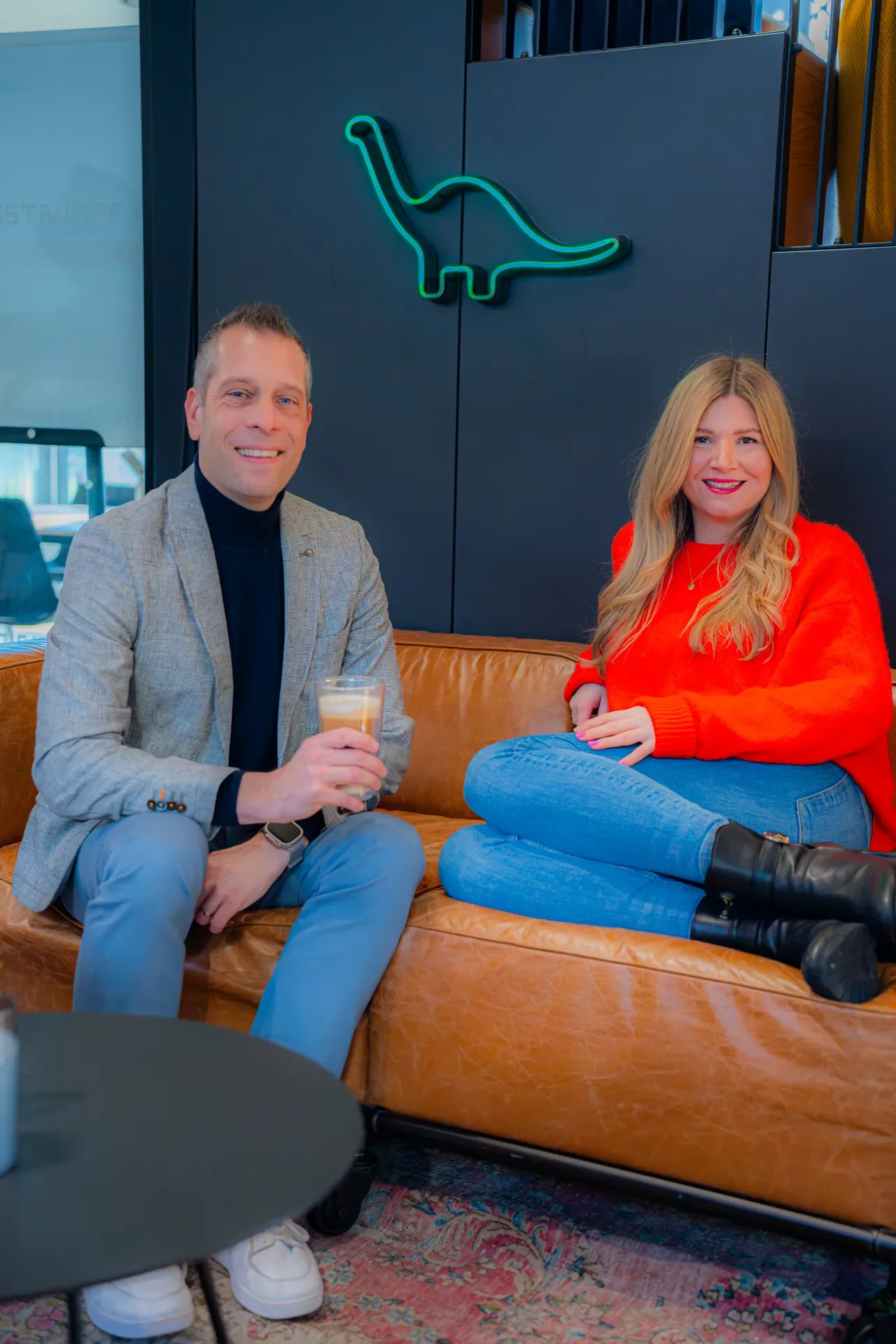 Zwei Ansprechpersonen des Campus Space auf dem Sofa unter dem Neon-Dino